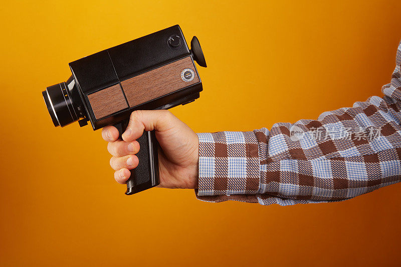 电影摄影师拿着老式模拟Super8, 8毫米电影摄影机在黄色背景。把相机对准枪